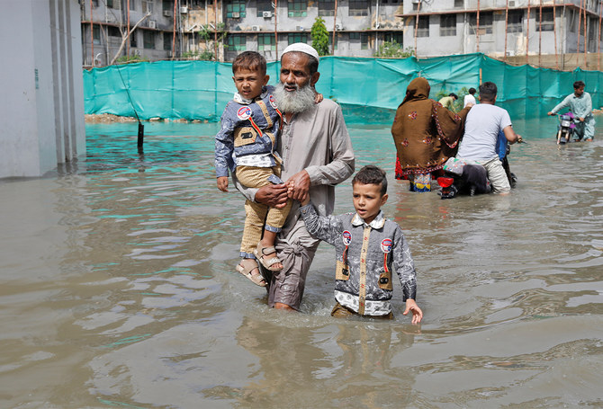 A man carrying two children through floodwater in an urban street in Pakistan
