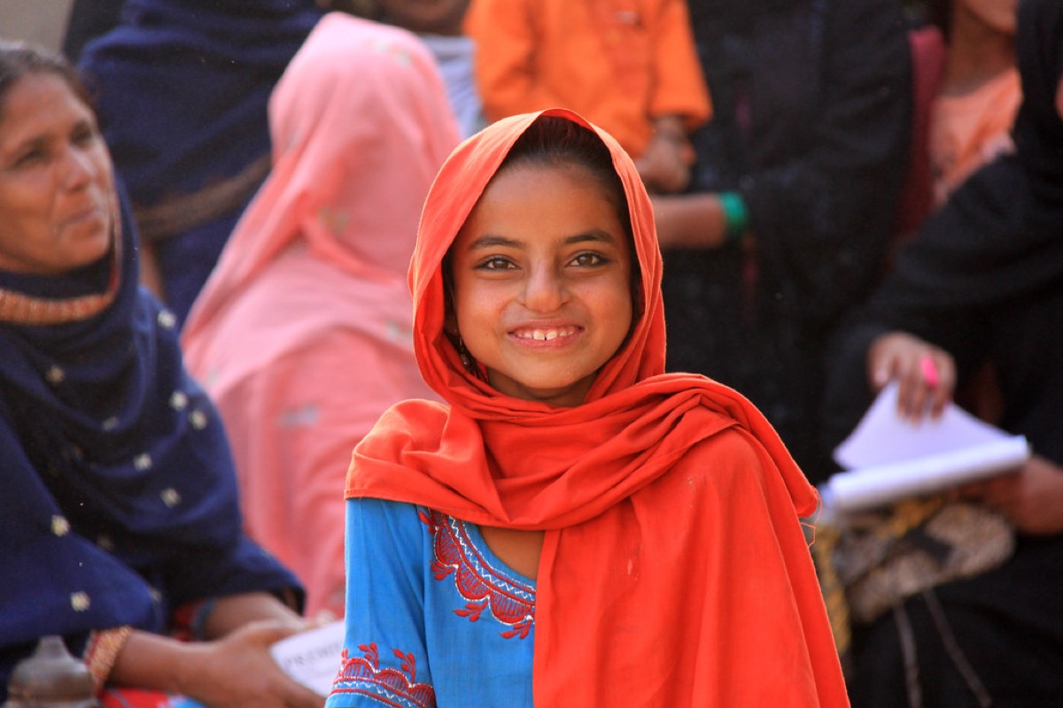 A young girl in an orange dupatta smiling during a community session